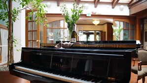 Een vleugelpiano in een goed verlichte kamer met houten balken, een potplant en een bloevas.