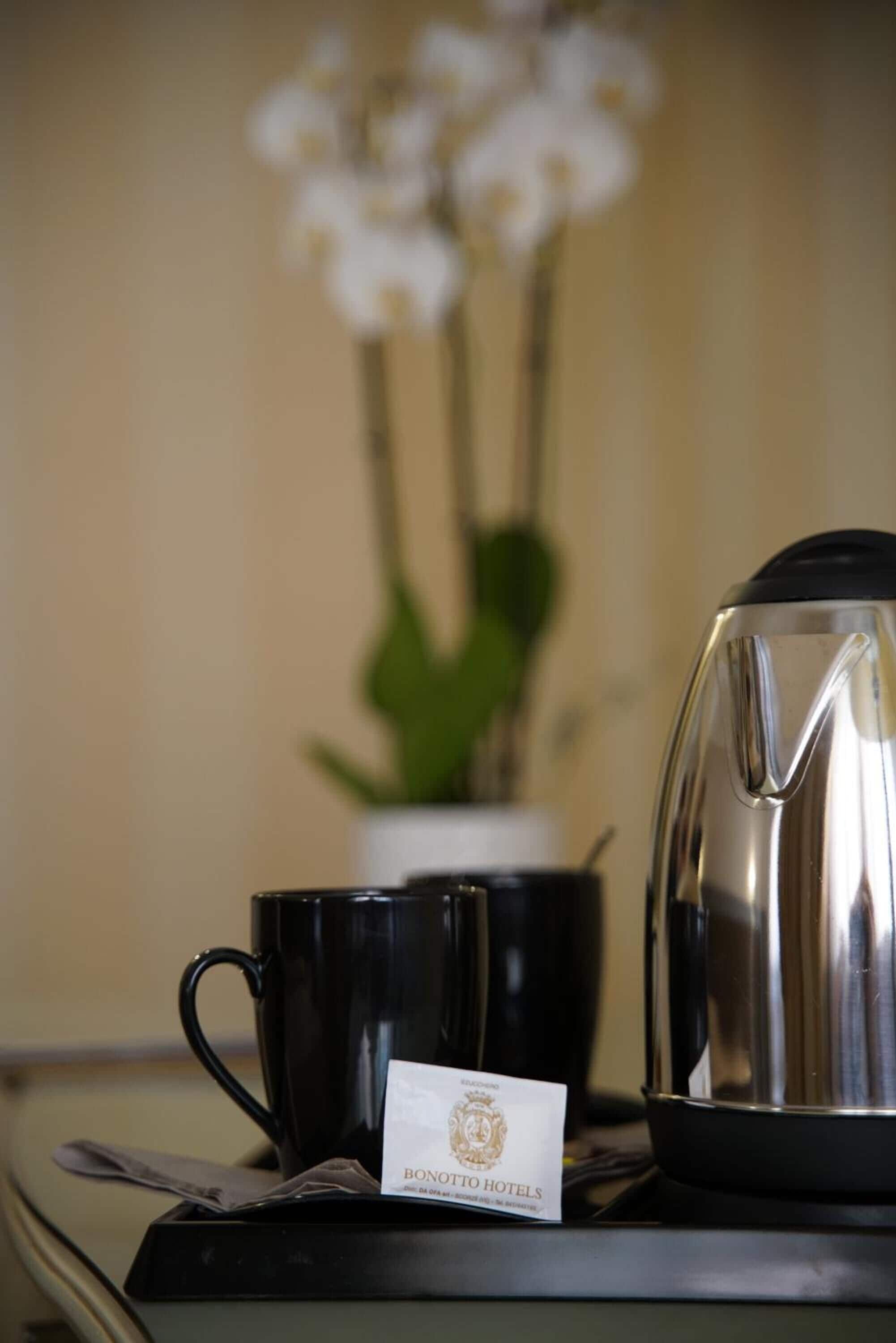 Una taza de café negro, una tetera plateada y una bolsita de té sobre una bandeja con una tarjeta de Bonitto Hotels.