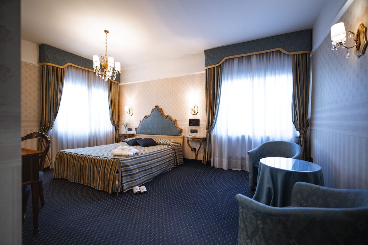 A hotel room with a large bed, a desk, a chair, and a small table.