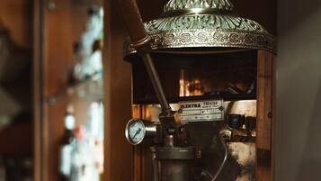 Une machine à expresso ancienne, dotée d’une finition en laiton et d’un boîtier en verre, posée sur un comptoir.