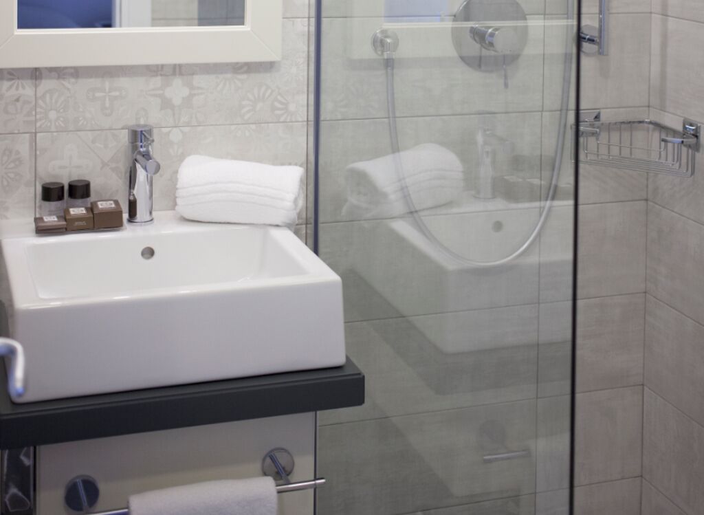 A bathroom with a white sink, a glass shower enclosure, and a tiled wall.