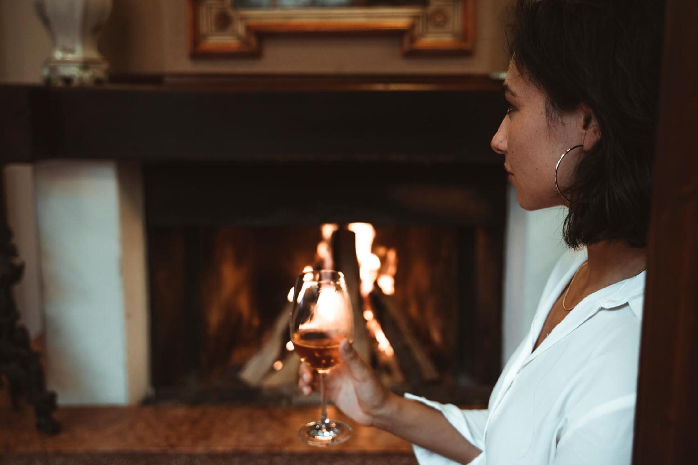 A person holding a glass of wine in front of a fireplace.