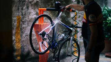 Une personne nettoie un vélo dans une ruelle étroite et humide à l’aide d’un tuyau d’arrosage.