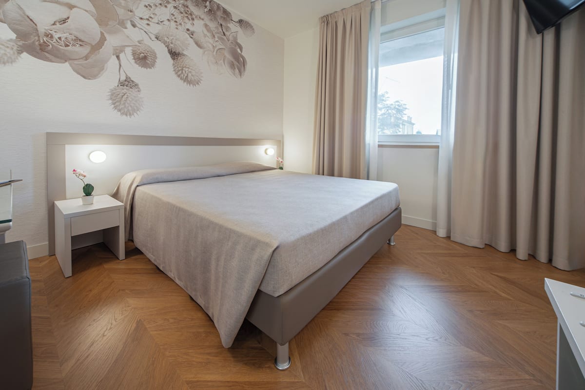 A modern bedroom with a bed, bedside table, and a window with curtains.