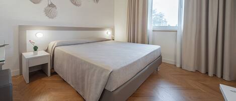 Un dormitorio moderno con cama, mesita de noche y ventana con cortinas.
