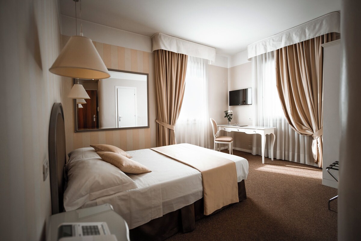 A hotel room with a bed, desk, chair, and a television.