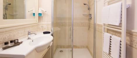 Un baño con ducha de vidrio, lavamanos con espejo y un perchero para toallas.