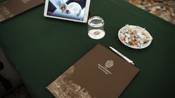 Una mesa con una tableta que muestra un menú, un vaso de agua, un plato de comida, un bolígrafo y un folleto titulado 'Bonotto Hotels'.