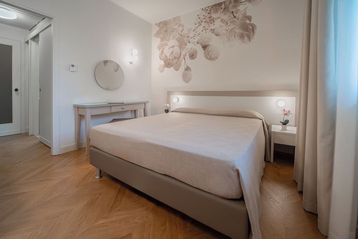 A bedroom with a bed, bedside tables, a desk, and a wall-mounted light fixture.