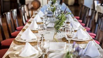 Une longue table à manger, dressée avec des serviettes blanches, des assiettes et des verres à vin, et un vase rempli de verdure placé au centre.