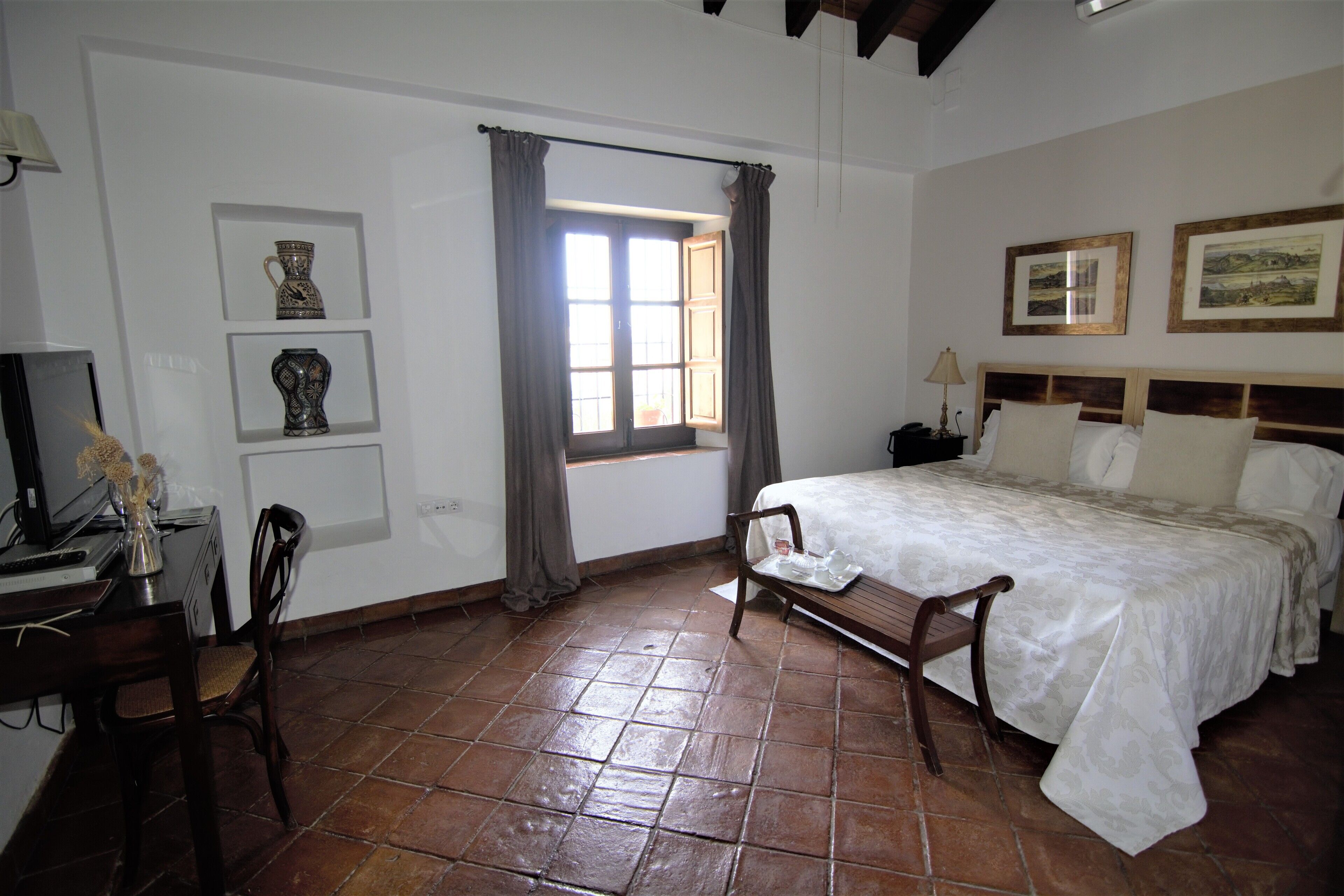 Un dormitorio con cama, escritorio, silla, ventana con cortinas e imágenes enmarcadas en la pared.