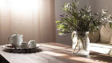 Une table en bois sur laquelle se trouvent une théière blanche, des tasses et des soucoupes, ainsi qu'un vase en verre transparent contenant des plantes vertes.