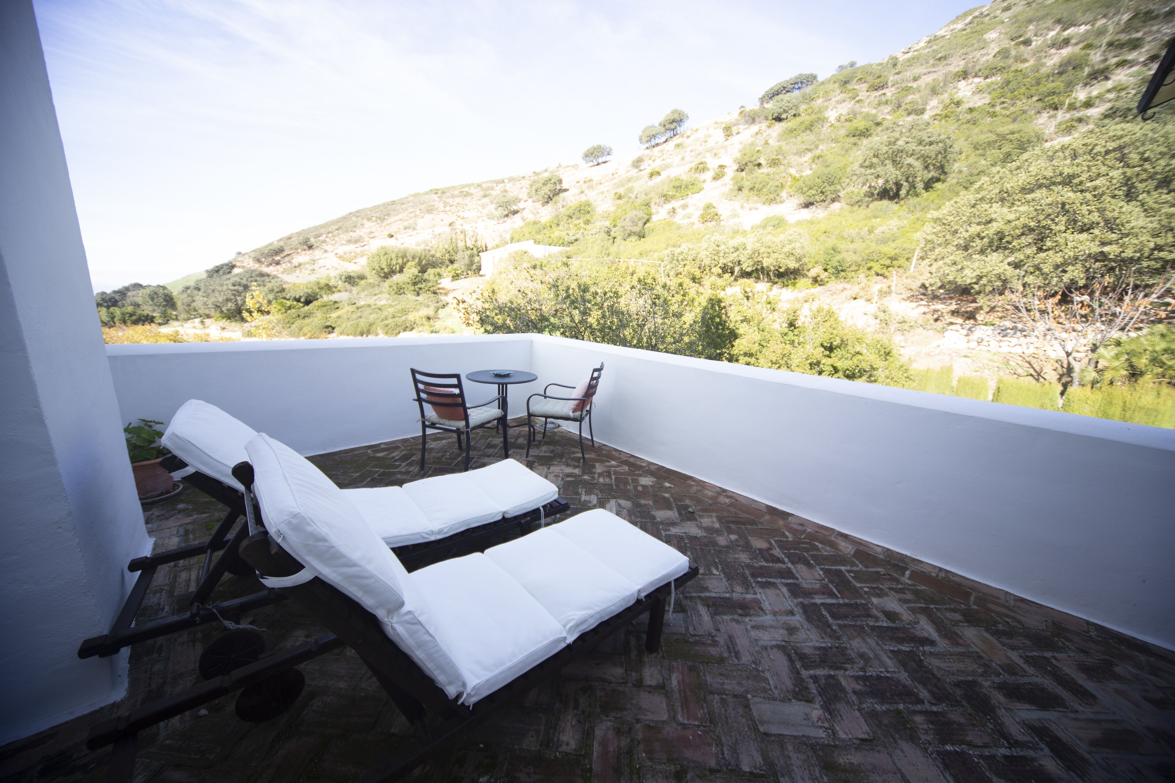 A balcony with two sun loungers and a small table, overlooking a hilly landscape.