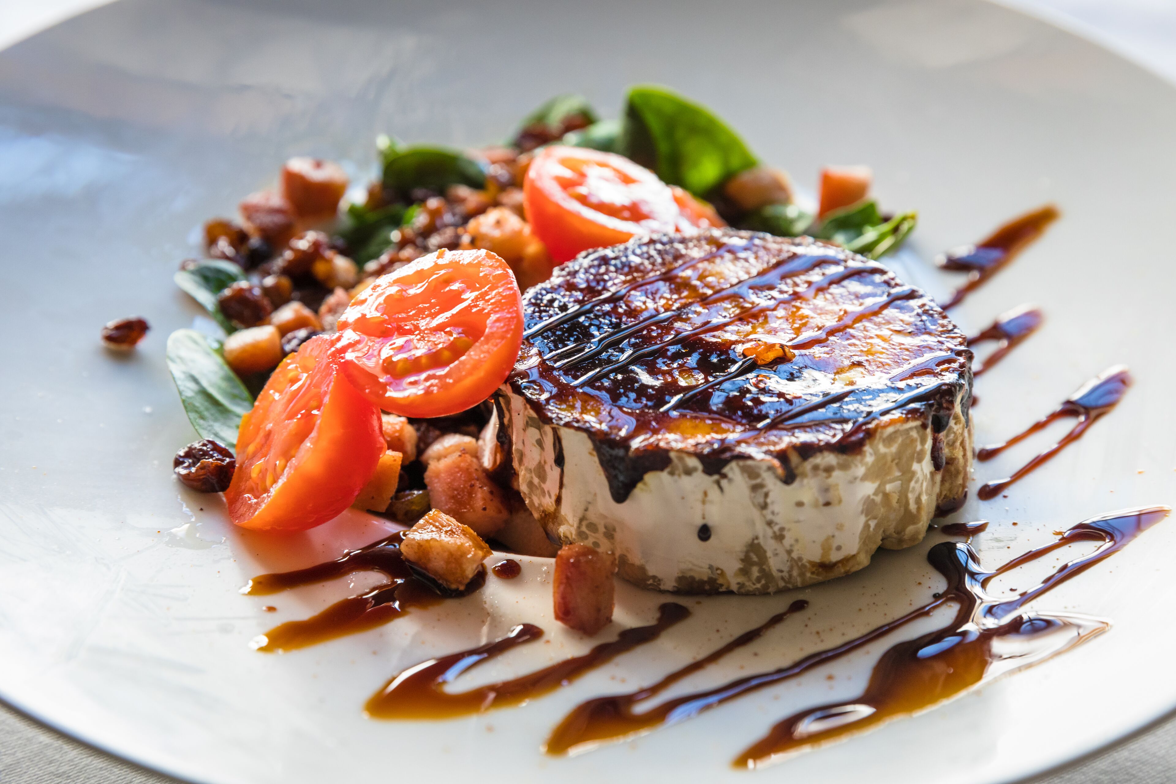 Une assiette avec un sandwich au fromage grillé, des tranches de tomates et un filet de sauce.