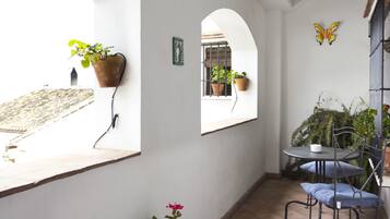 A small, enclosed patio area with a round table and chairs, potted plants, and a butterfly decoration on the wall.