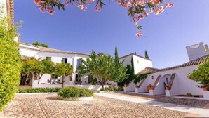 A courtyard with cobblestone paths, white buildings, and flowering trees. - Hotel Boutique Molino del Arco (Ronda)