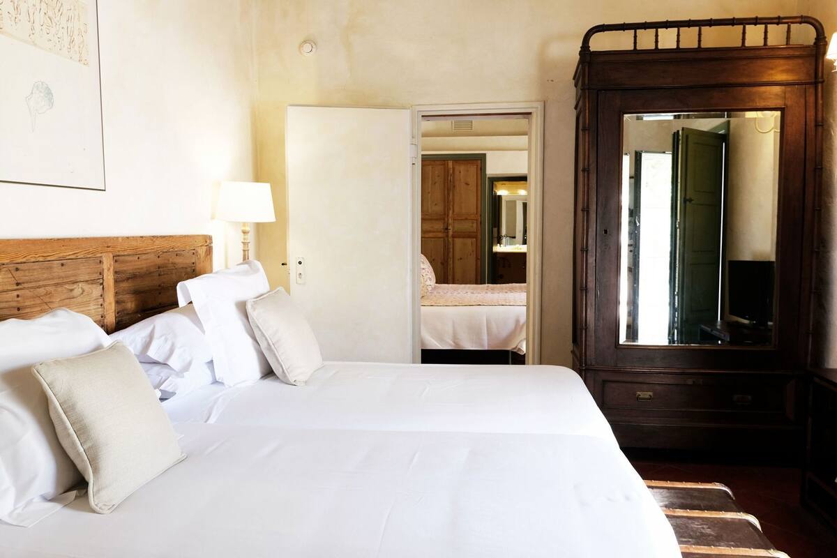 Ein Hotelzimmer mit einem großen Bett, einem Holz-Kopfteil, einem Spiegel und einer Tür zu einem anderen Raum.