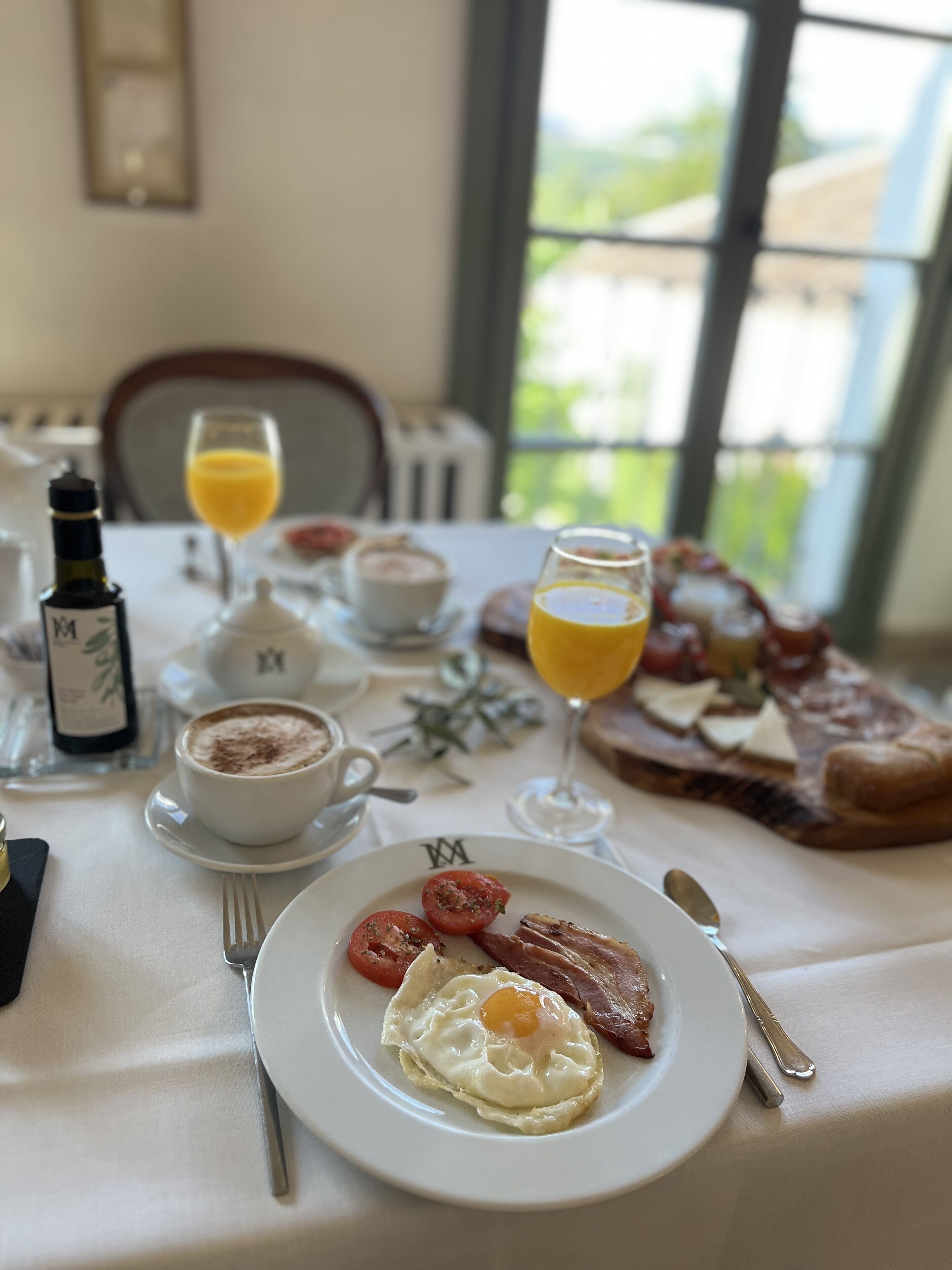 A breakfast table with a plate of eggs, tomatoes, and bacon, a glass of orange juice, a cup of coffee, and a slice of toast.