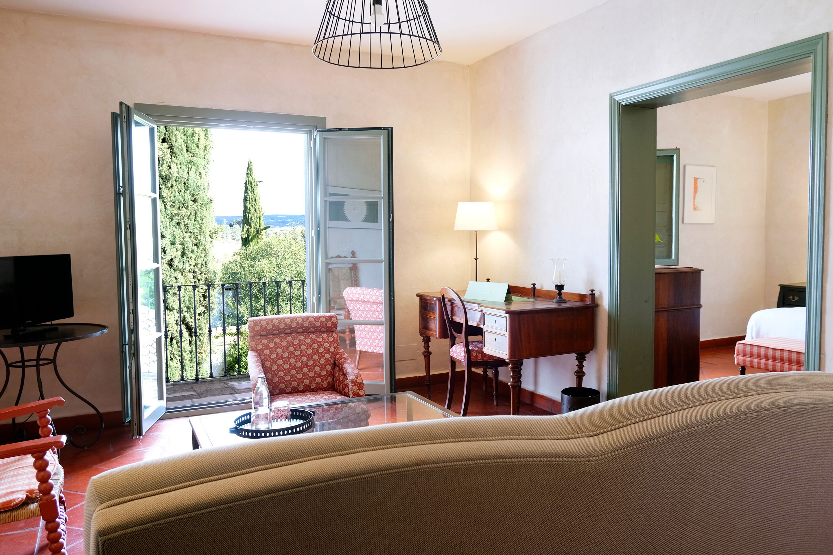 A hotel room with a balcony, a desk, a chair, a TV, and a bed.