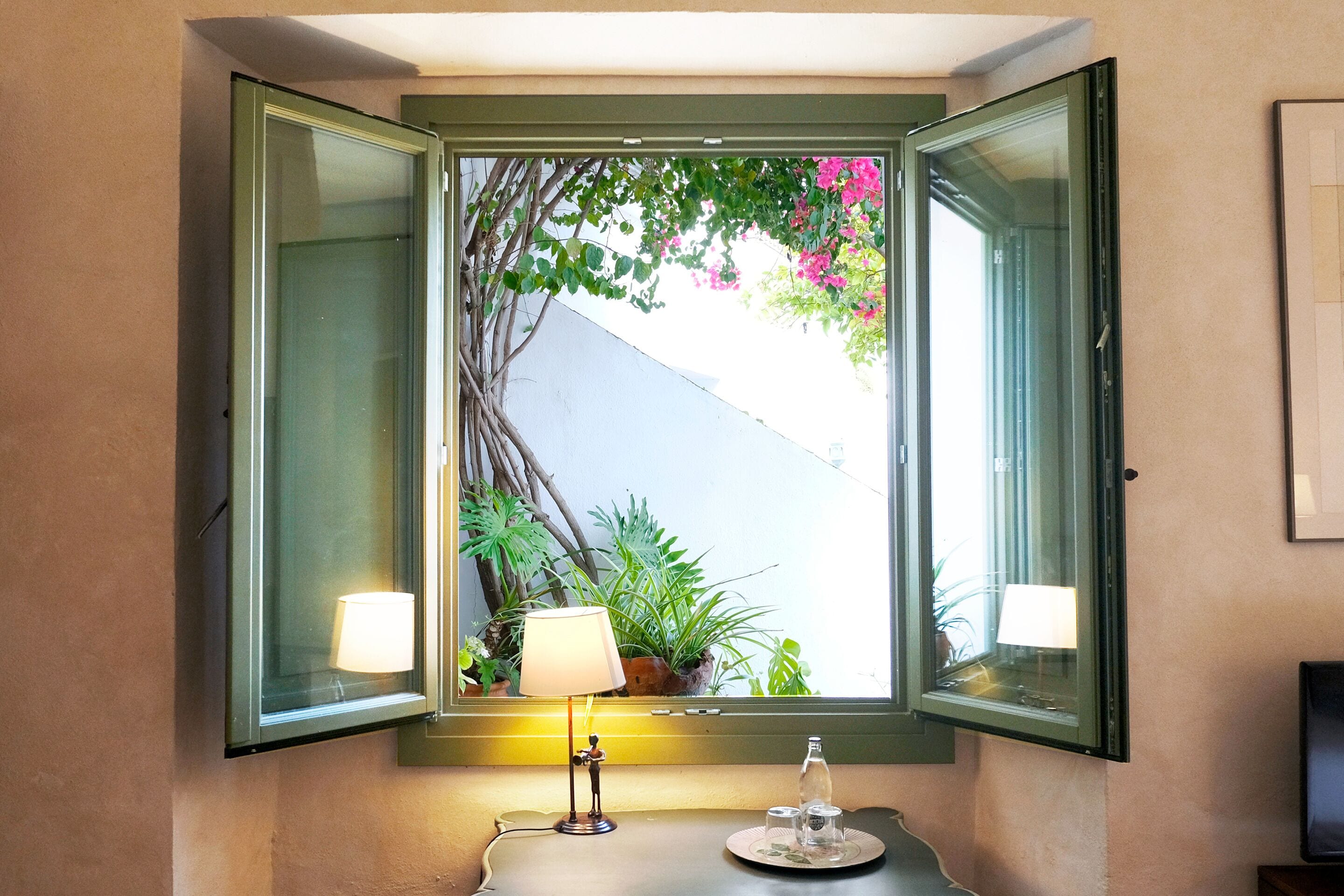 Un baño con ventana, una lámpara y una mesita con una botella y vasos.