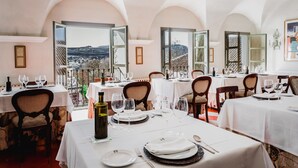 A dining area with tables set for a meal, large windows with a view of a mountainous landscape, and a chandelier on the wall. - Hotel Boutique Molino del Arco (Ronda)
