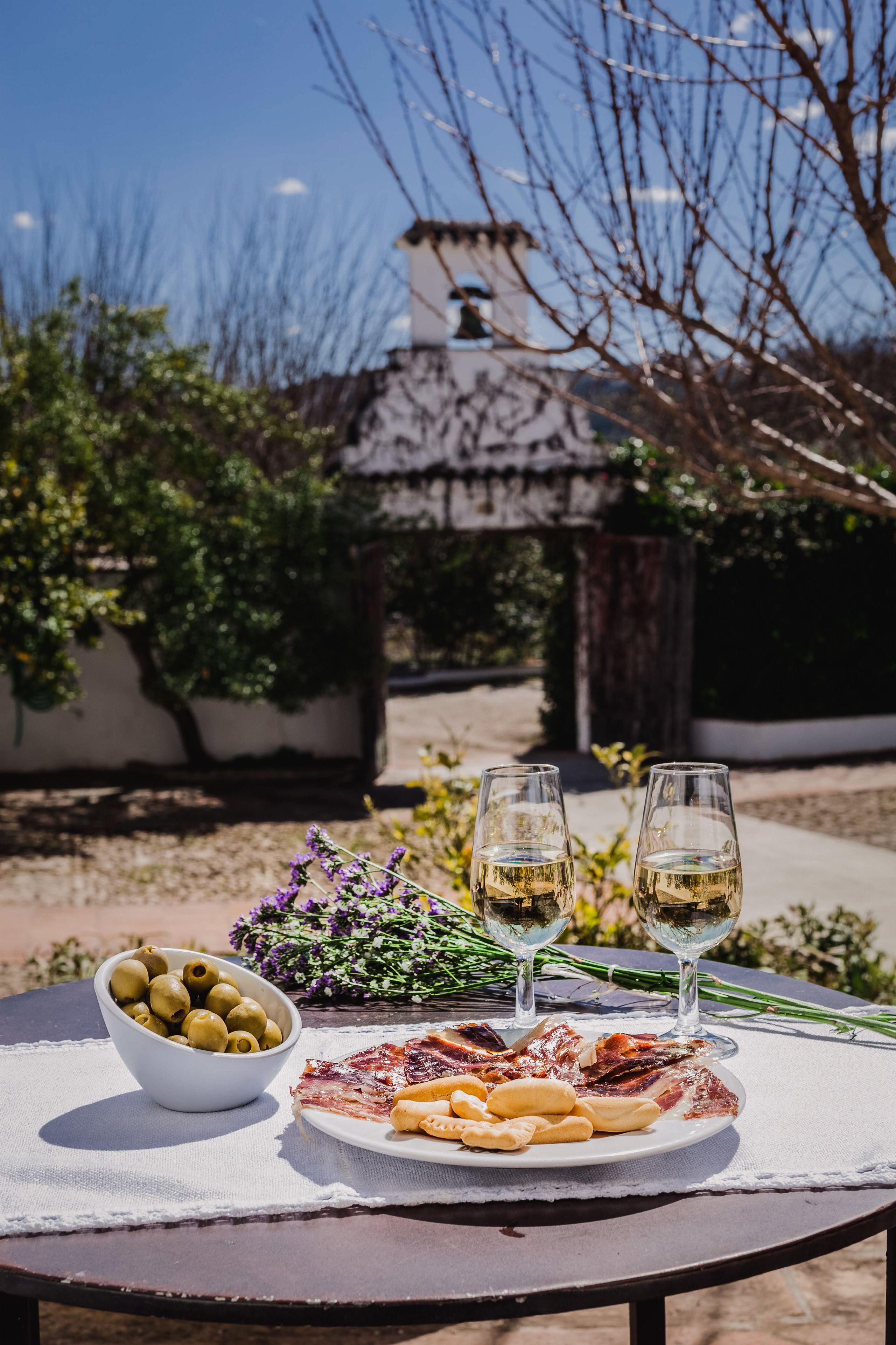 A table with a plate of food, two glasses of wine, and a bowl of olives.