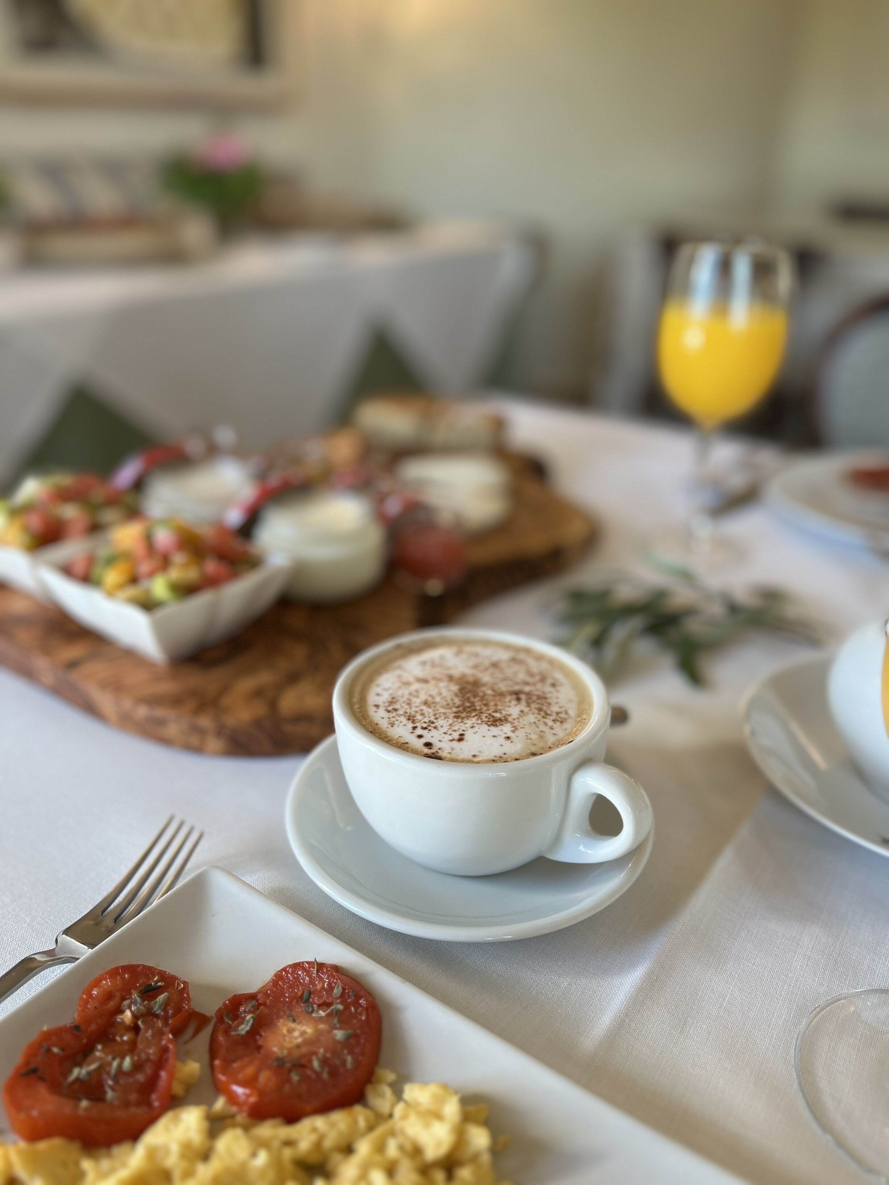 Un desayuno con una taza de café, huevos revueltos y una ensalada de frutas sobre una tabla de madera.
