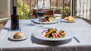 A dining table with plates of food, wine glasses, and a bottle, set against a scenic view of a landscape with hills and a church spire. - Hotel Boutique Molino del Arco (Ronda)