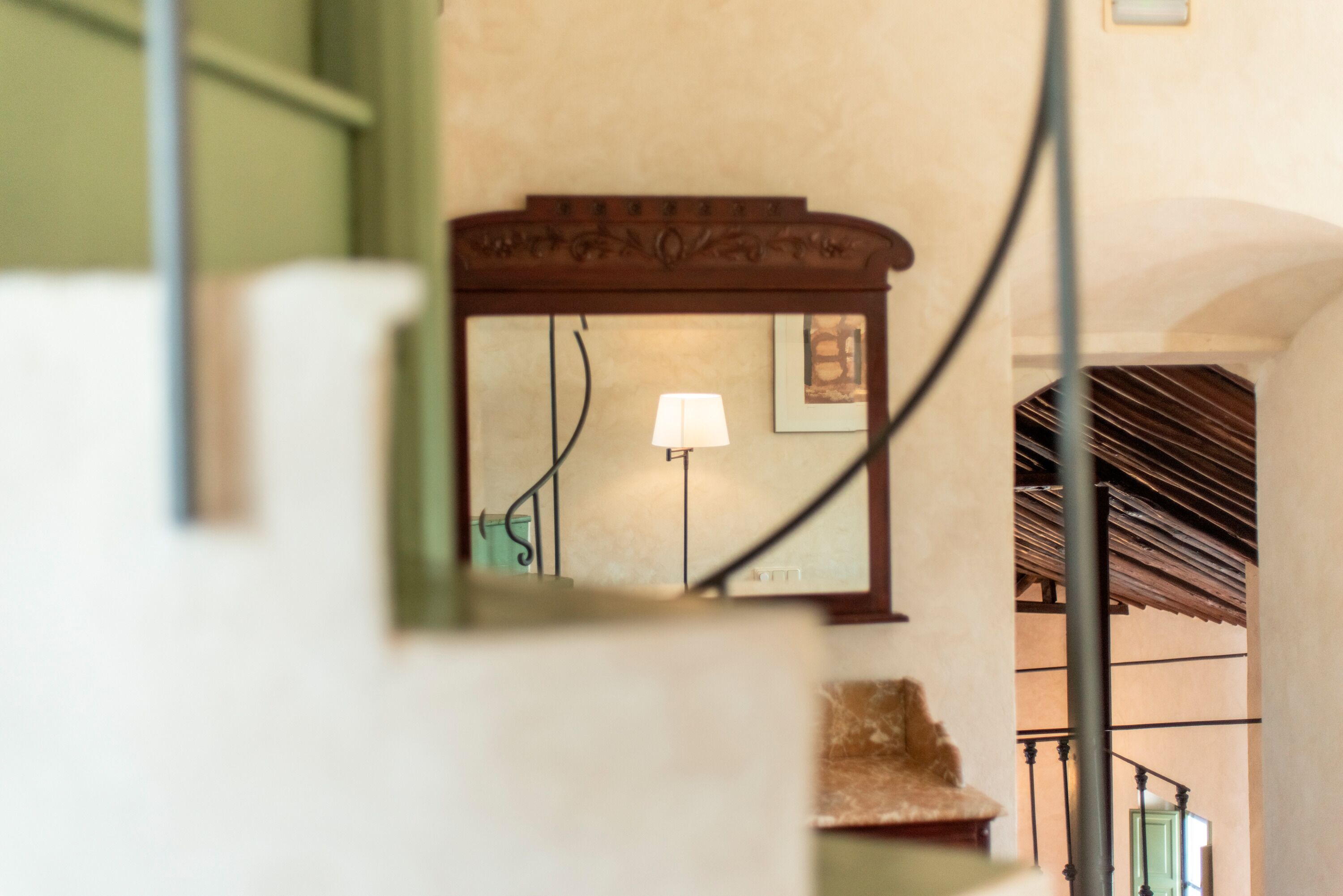 Una escalera con barandilla de madera y un espejo fijado a la pared que refleja una lámpara y un cuadro enmarcado.