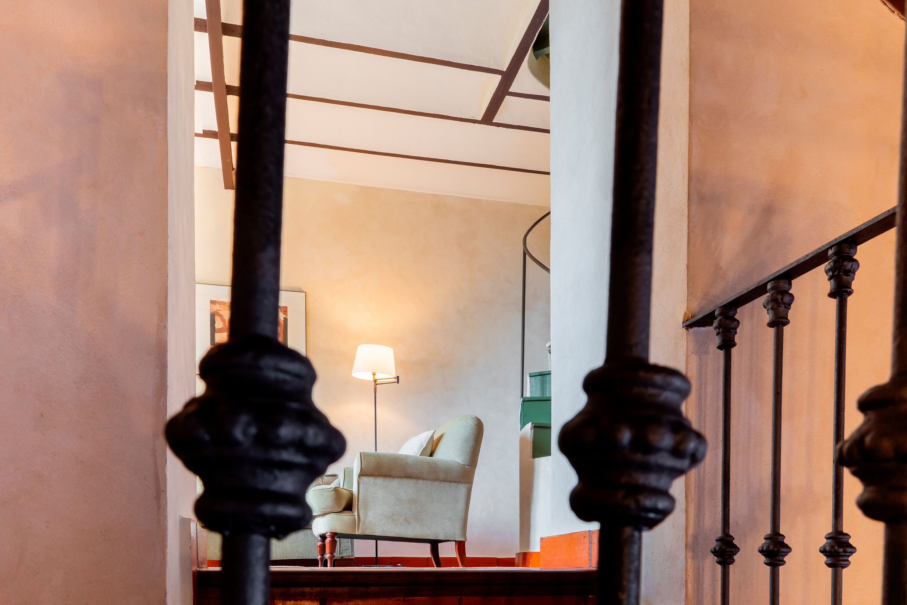 A staircase with ornate balusters, a white armchair, and a floor lamp in the background.