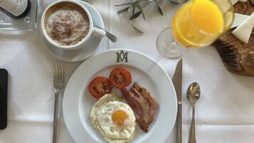 A breakfast setting with a plate of eggs, bacon, and tomatoes, a cup of coffee, and a glass of orange juice.