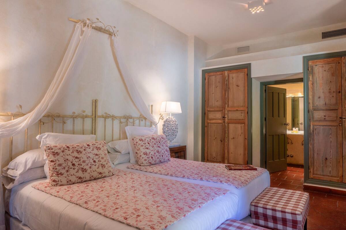 Ein Schlafzimmer mit zwei Betten, einem Himmelbett, einem Nachttisch mit Lampe und Holztüren.