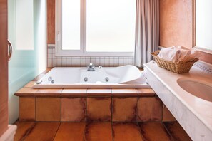 A bathroom with a large freestanding bathtub, a wicker basket with towels, and a window with curtains.