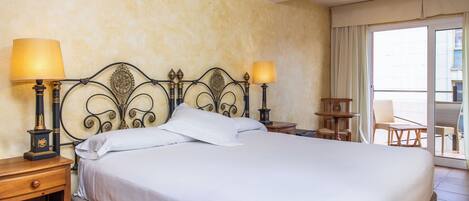 A neatly made bed with white linens, two bedside lamps, a wooden nightstand, and a chair by a sliding glass door.