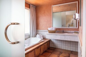Une salle de bain avec une baignoire, un lavabo, un miroir et une fenêtre avec des rideaux.
