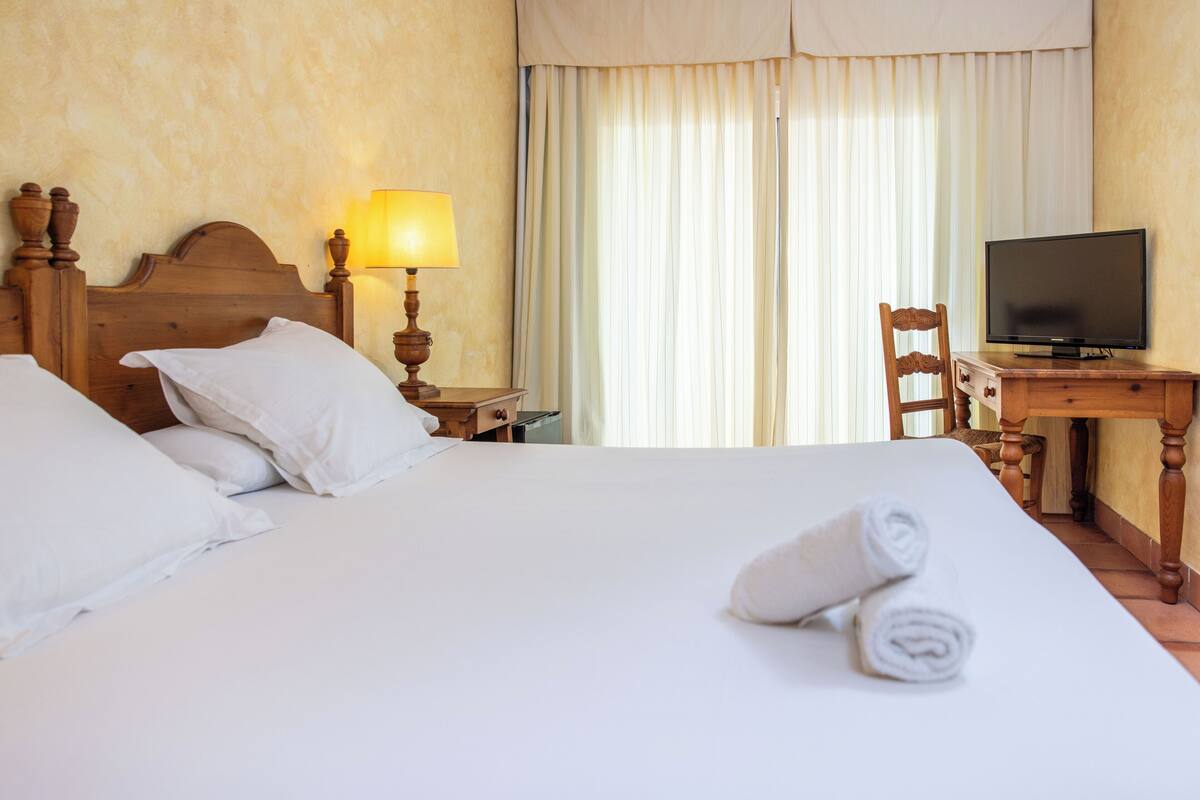 Una habitación de hotel con una cama, un escritorio con televisor, una lámpara y una silla.