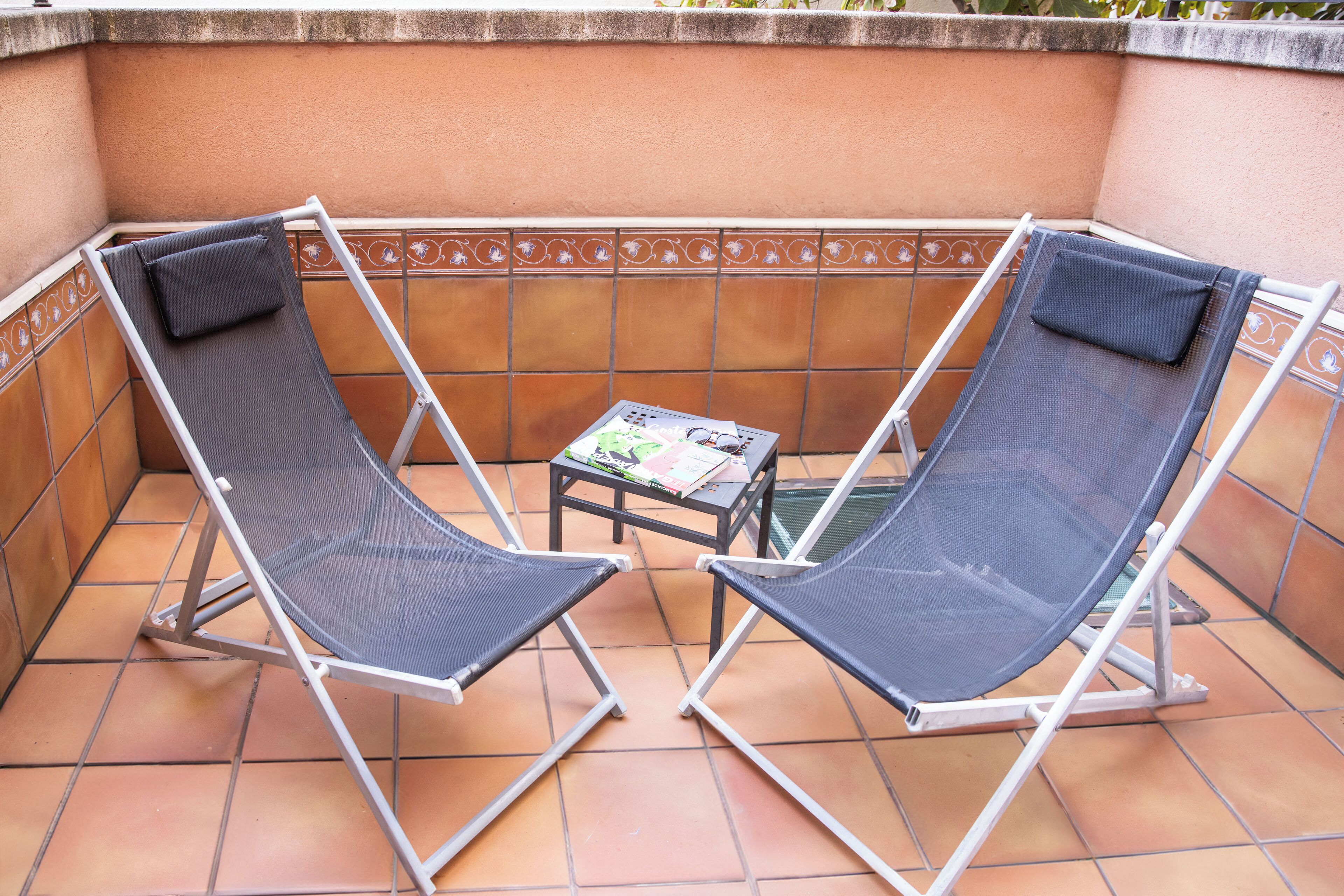 Dos sillones con cojines en un patio empedrado con una mesita y una revista.