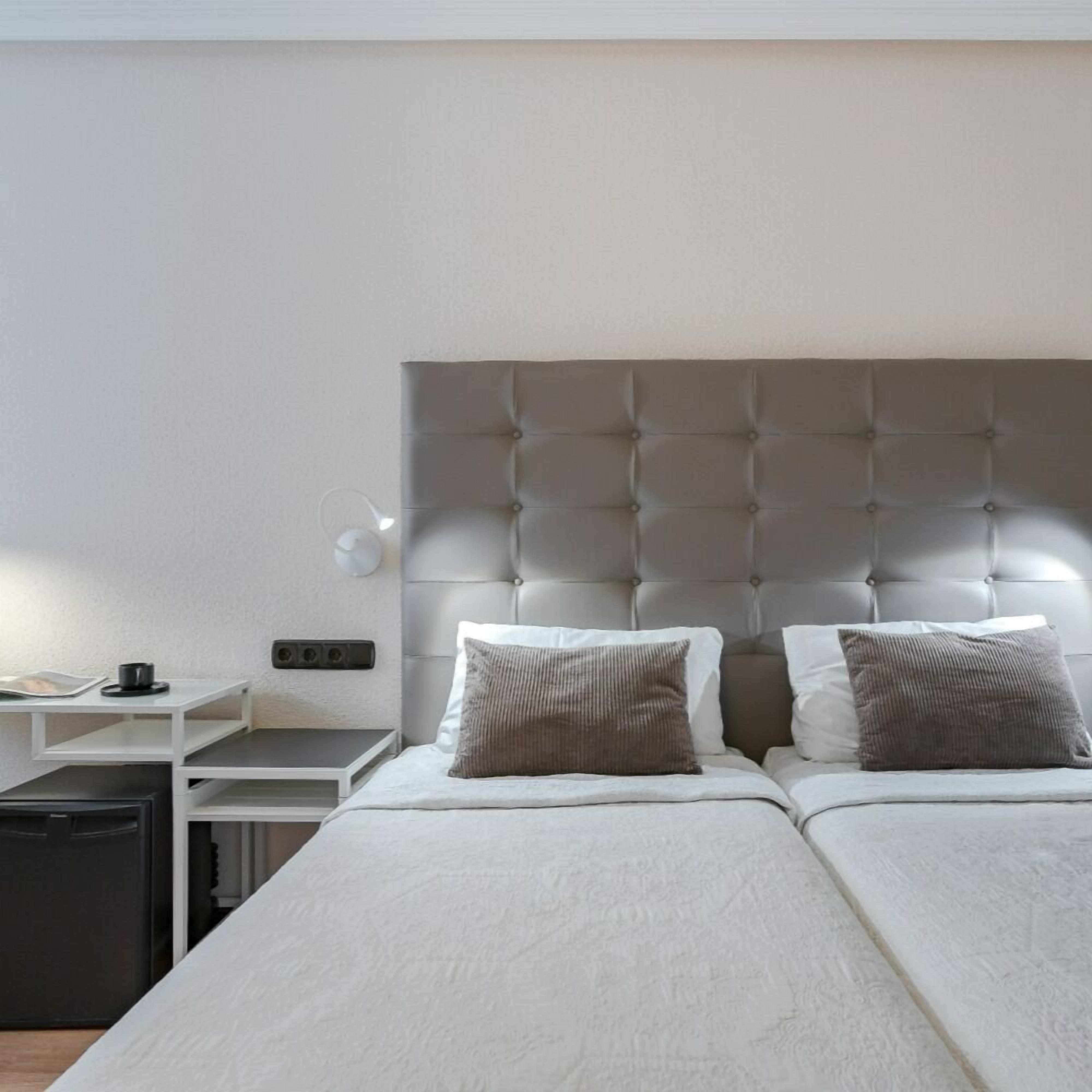 Habitación de hotel con dos camas, una mesita de noche, una lámpara y un escritorio pequeño con una silla.