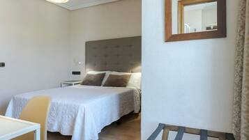 A hotel room with a bed, a bedside table, a chair, a hanging light fixture, and a mirror on the wall.