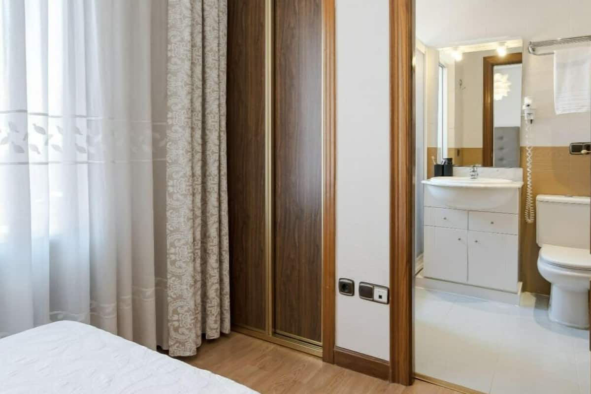 A hotel room with a bed, a wooden wardrobe, and a bathroom visible through an open door.