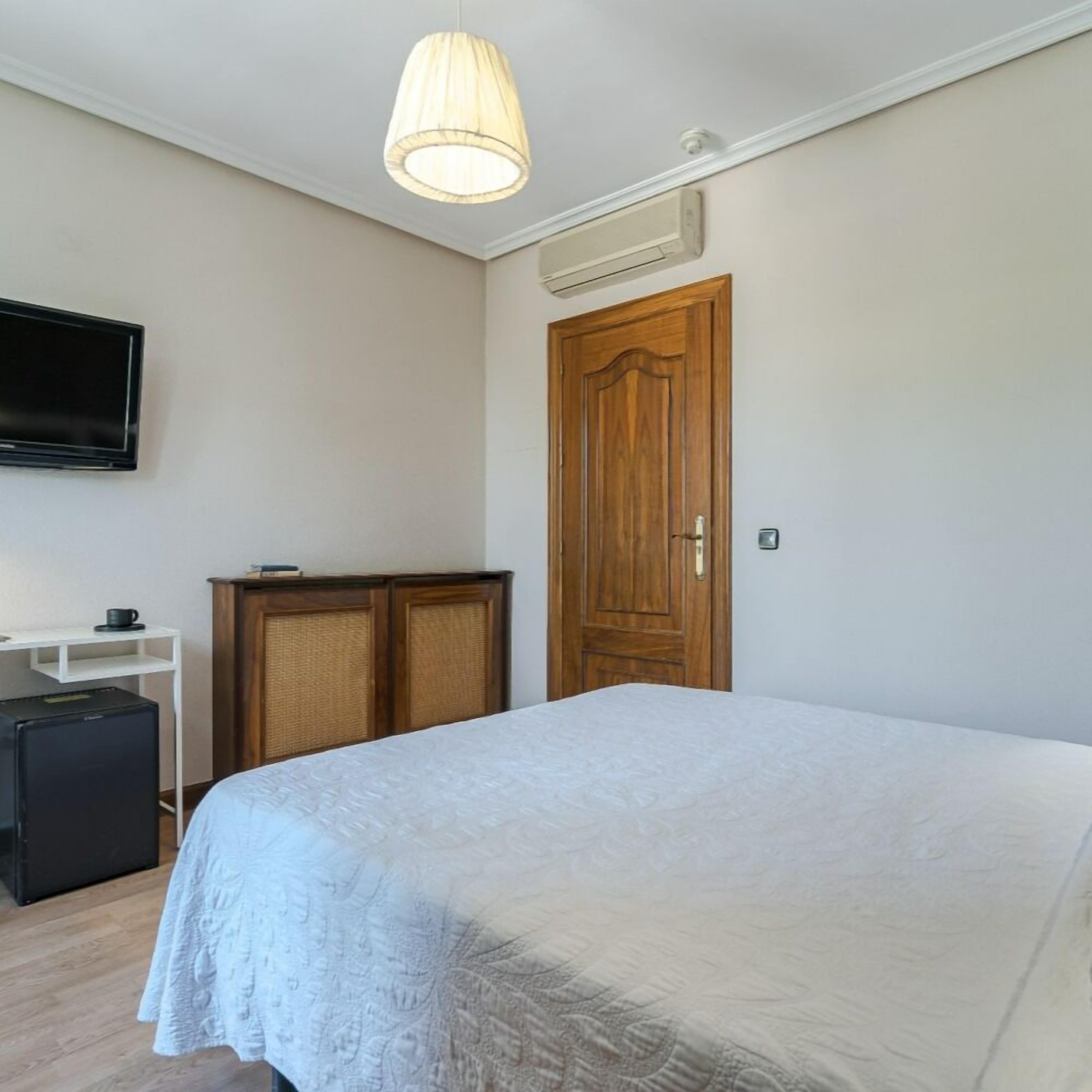 A bedroom with a bed, a TV mounted on the wall, a wooden door, and a small table with a cup.