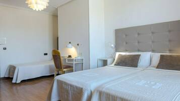 A hotel room with a large bed, a smaller bed, a desk, a chair, and a hanging light fixture.