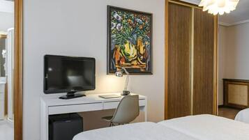Une chambre d’hôtel avec un lit, un bureau équipé d’un ordinateur, une télévision, un tableau au mur et un luminaire au plafond au design original.
