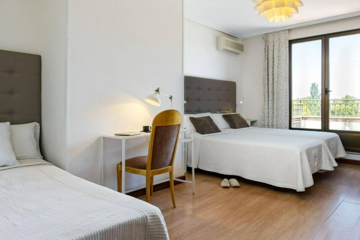 A hotel room with two beds, a desk, a chair, and a large window with a view.