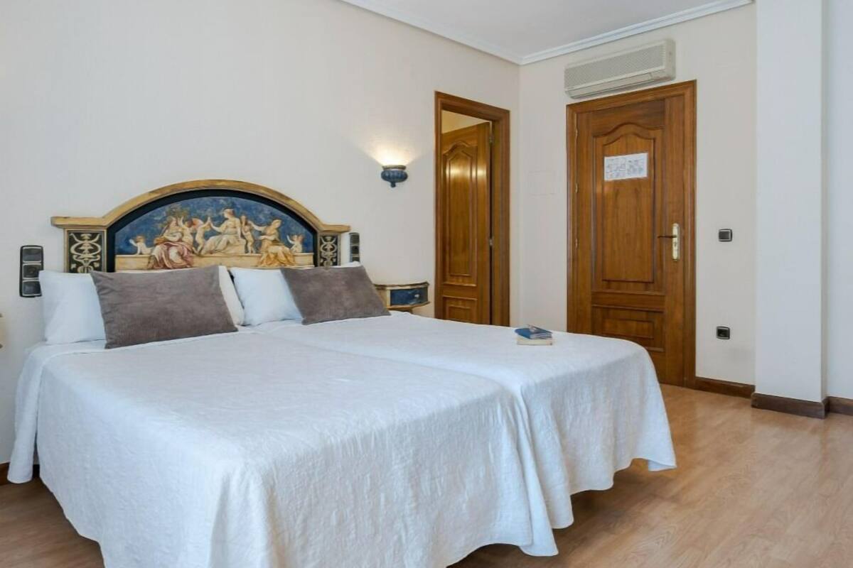 A bedroom with a large bed, a decorative headboard, a nightstand, and a wall-mounted lamp.
