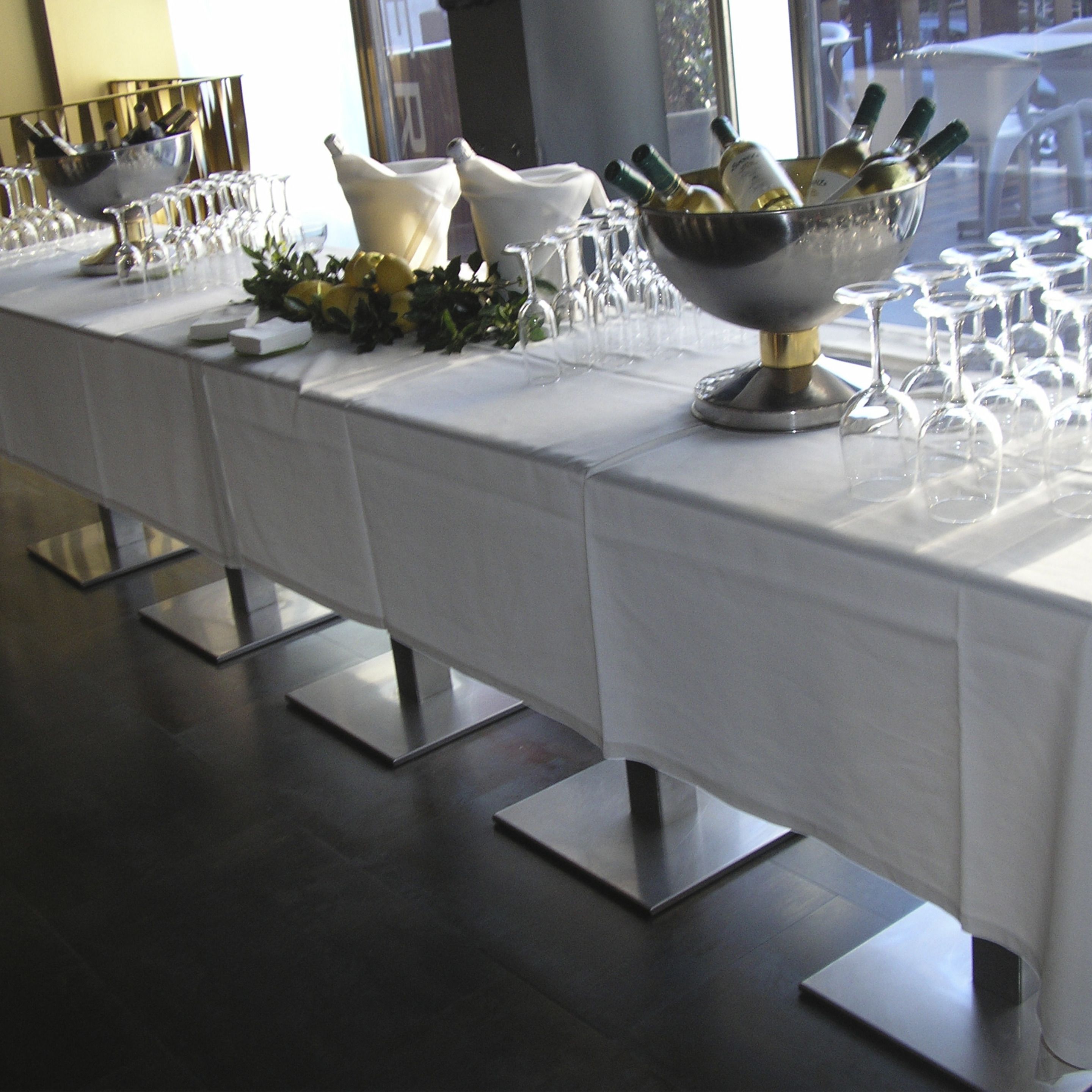 Una larga mesa dispuesta con botellas de vino, copas y un cuenco de flores.