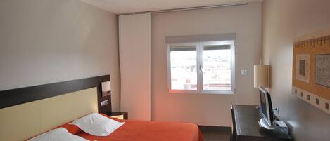 Habitación de hotel con cama, escritorio, silla, lámpara y ventana.