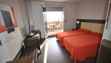 Habitación de hotel con dos camas, un escritorio, una silla, un televisor y un balcón con sillas.