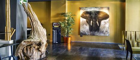 A lobby with a large wooden sculpture, a potted plant, and a wall-mounted elephant artwork.