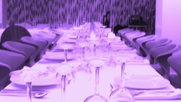 Een lange tafel gedekt met wijnglazen en borden, waarschijnlijk in een balzaal of evenementenruimte.
